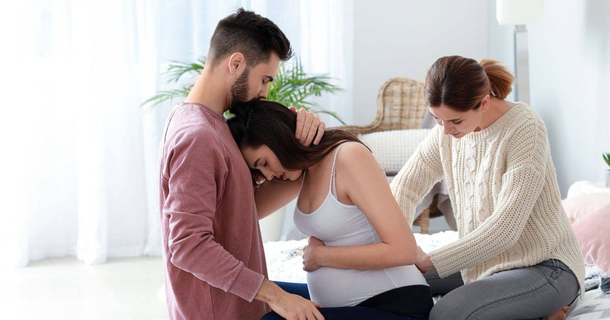 Doula providing back support to woman in labor and partner