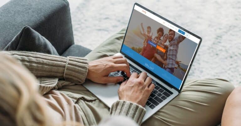 Person sitting comfortably at home browsing a travel website on their laptop, which displays images of happy travelers