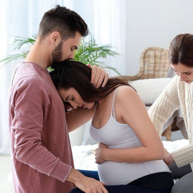 Doula providing back support to woman in labor and partner