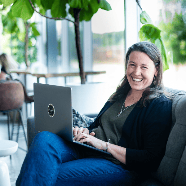 Sarah Juliusson The Website Doula sitting on couch with laptop looking at camera and smiling