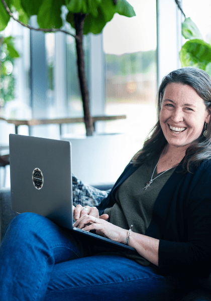 Sarah Juliusson The Website Doula sitting on couch with laptop looking at camera and smiling